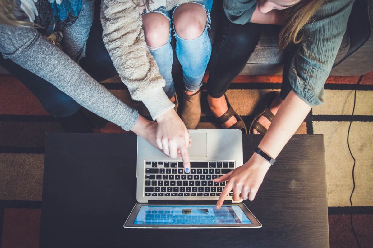 A group of girls sit in front of a laptop and point with their fingers